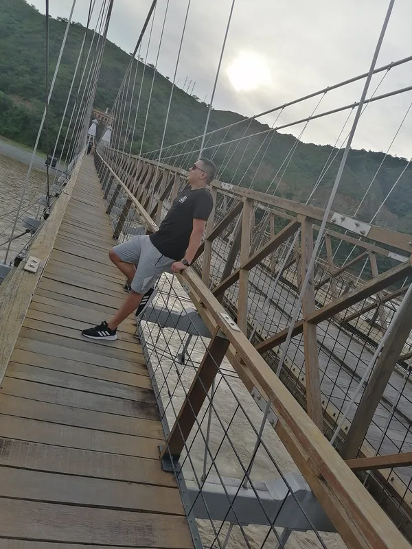 Un viajero cruza un puente colgante de madera entre montañas